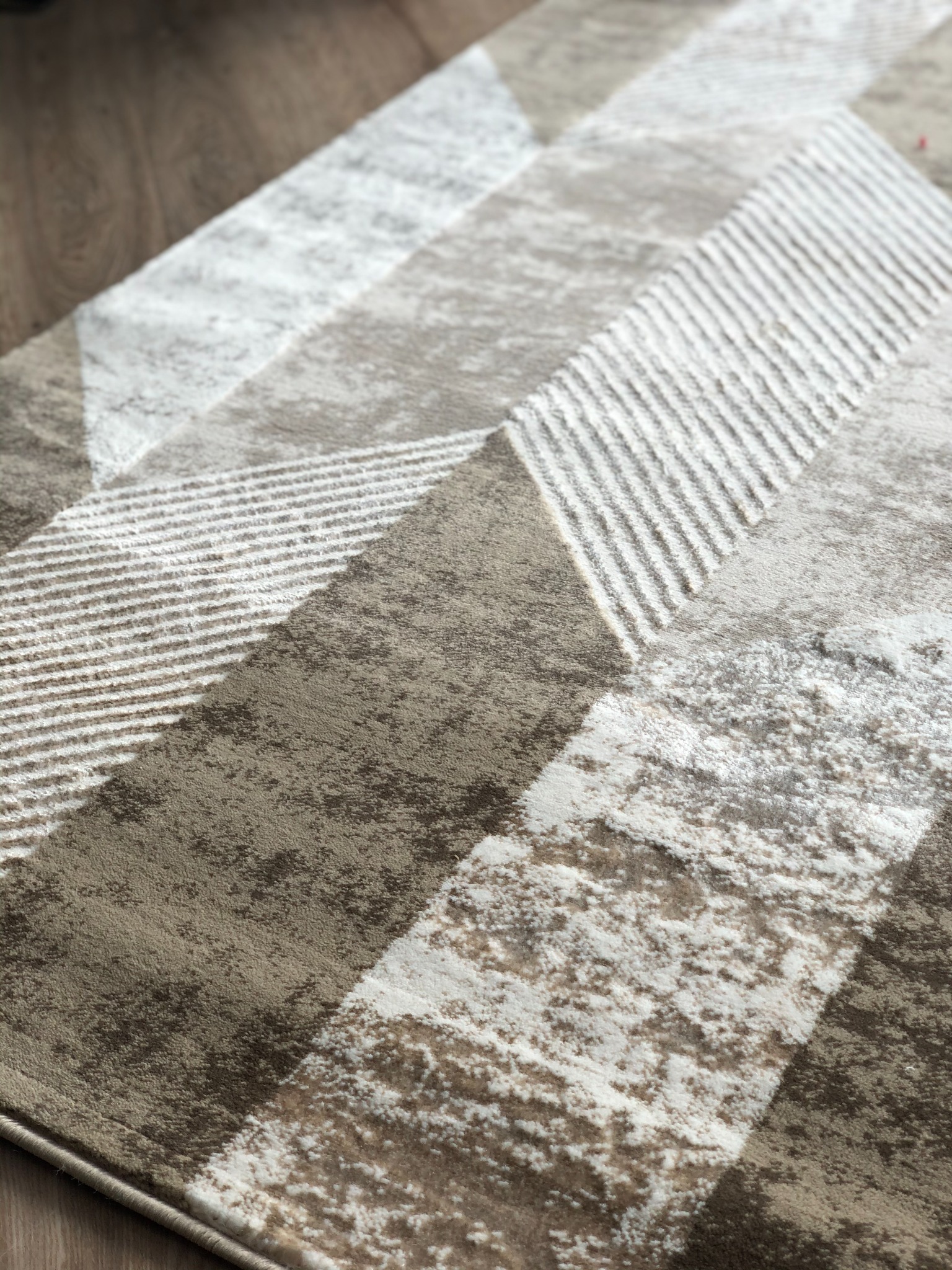 Beżowo-biały dywan z geometrycznym wzorem na drewnianej podłodze, widok z góry, ostre światło.