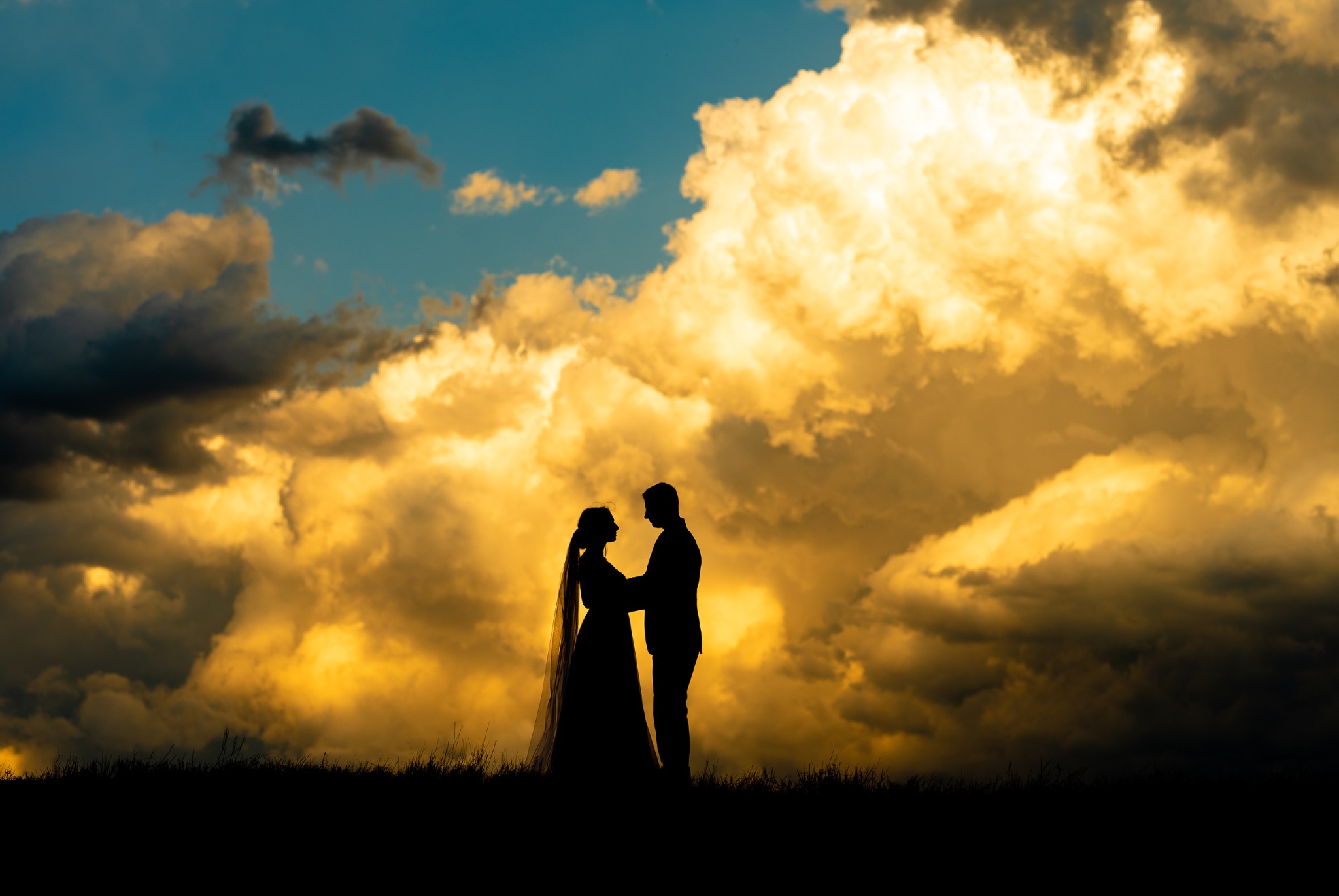 Sylwetki pary młodej na tle dramatycznego, złocistego nieba z chmurami.