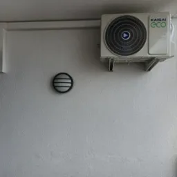 Zewnętrzna jednostka klimatyzatora Kaisai Eco zamontowana na balkonie, widoczne przewody i lampa ścienna w tle.