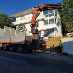 Dawid Ordon - Montaż prefabrykowanych elementów betonowych przy użyciu dźwigu Palfinger na budowie domu jednorodzinnego, dwóch pracowników w kamizelkach odblaskowych nadzoruje proces.