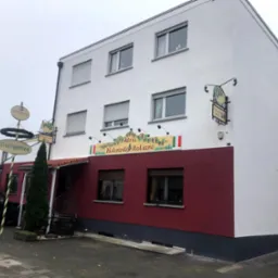 Dwupiętrowy budynek restauracji włoskiej z czerwonym dolnym pasem i białym górnym, widoczne szyldy i tablice informacyjne, zaparkowany samochód obok.