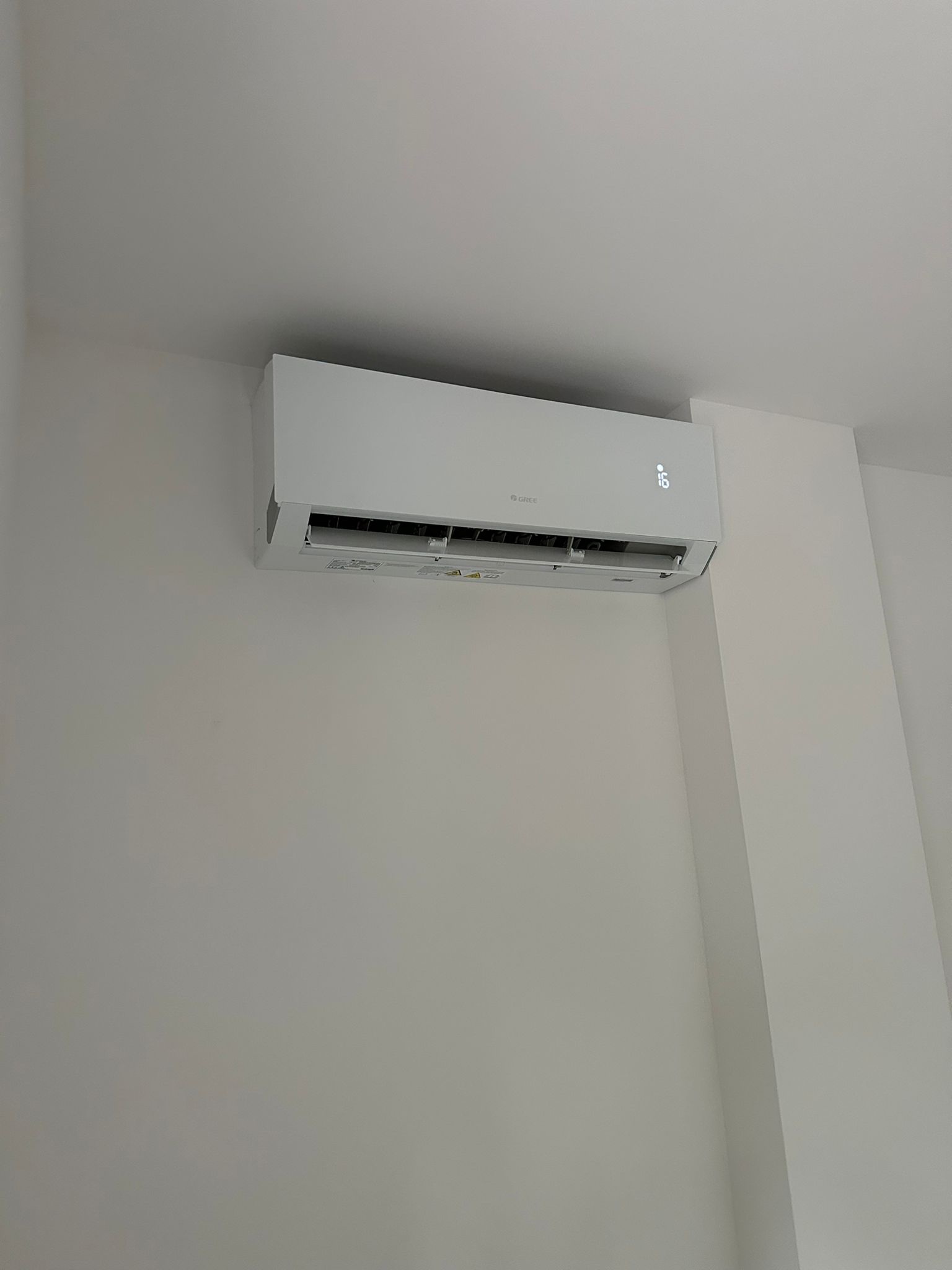 Biała klimatyzacja marki Gree zamontowana na białej ścianie w pomieszczeniu, wyświetlająca temperaturę 16 stopni.