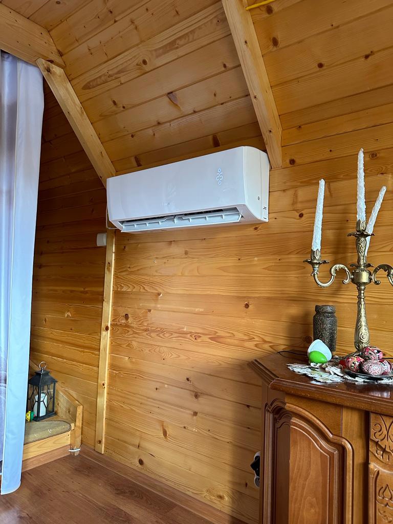 Biała klimatyzacja ścienna zamontowana w drewnianym domku, obok ozdobny świecznik i komoda.