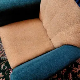 Fragment wyczyszczonego fotela z beżową tapicerką i turkusowymi bokami, leżącego na dywanie w orientalne wzory.