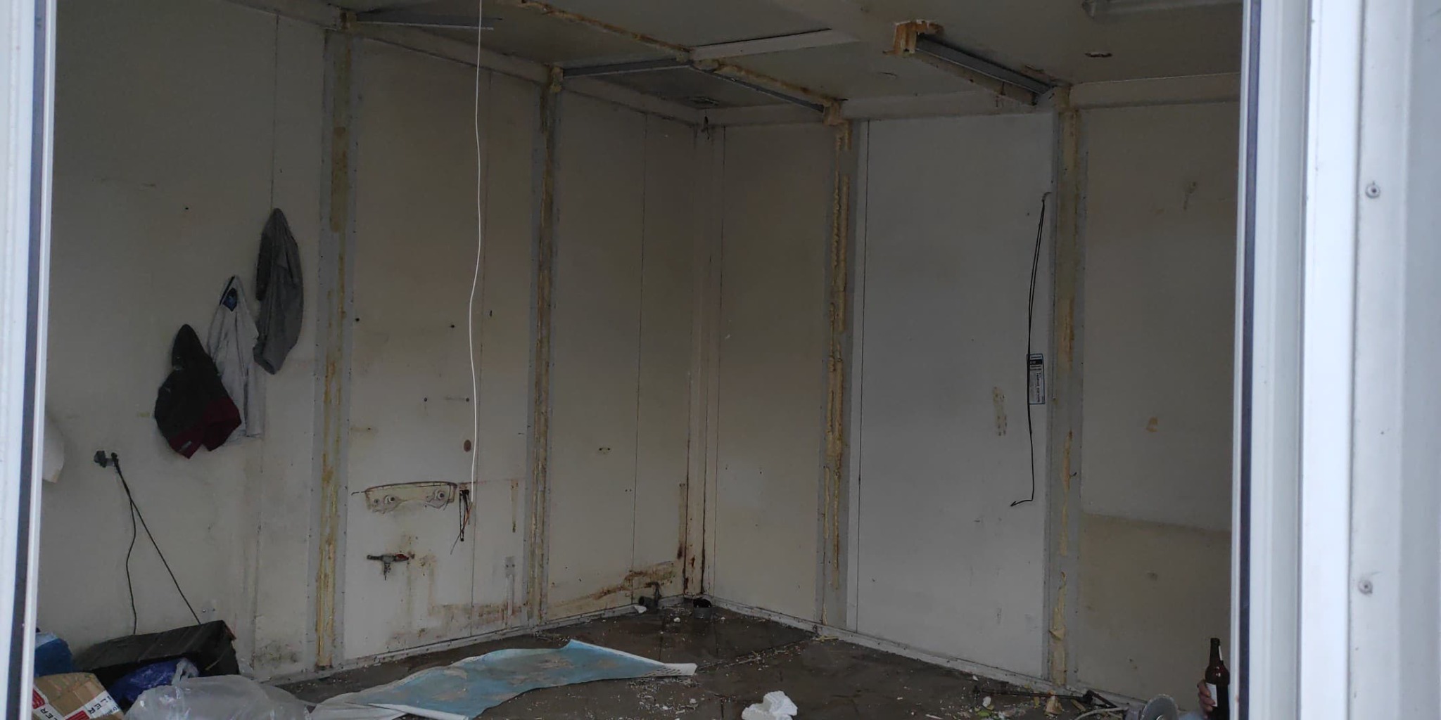 Wnętrze pomieszczenia w trakcie remontu: widoczne płyty karton gips, instalacje elektryczne, ślady po pracach budowlanych oraz resztki materiałów na podłodze.
