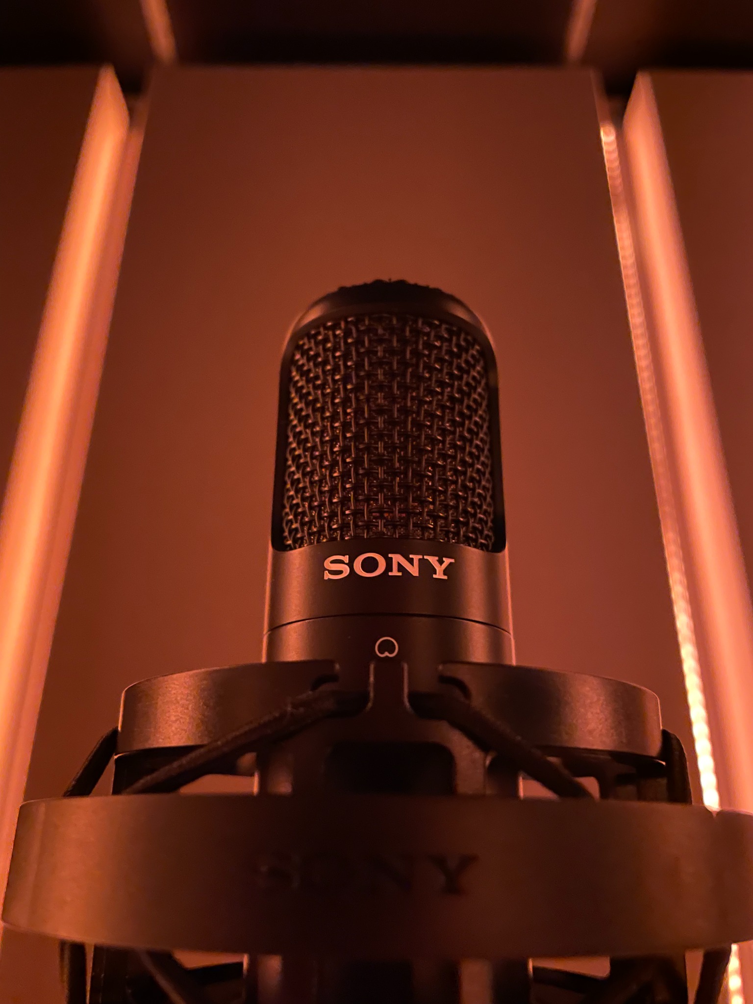 Pionowe ujęcie mikrofonu marki Sony na tle ciepłego, pomarańczowego oświetlenia studyjnego.