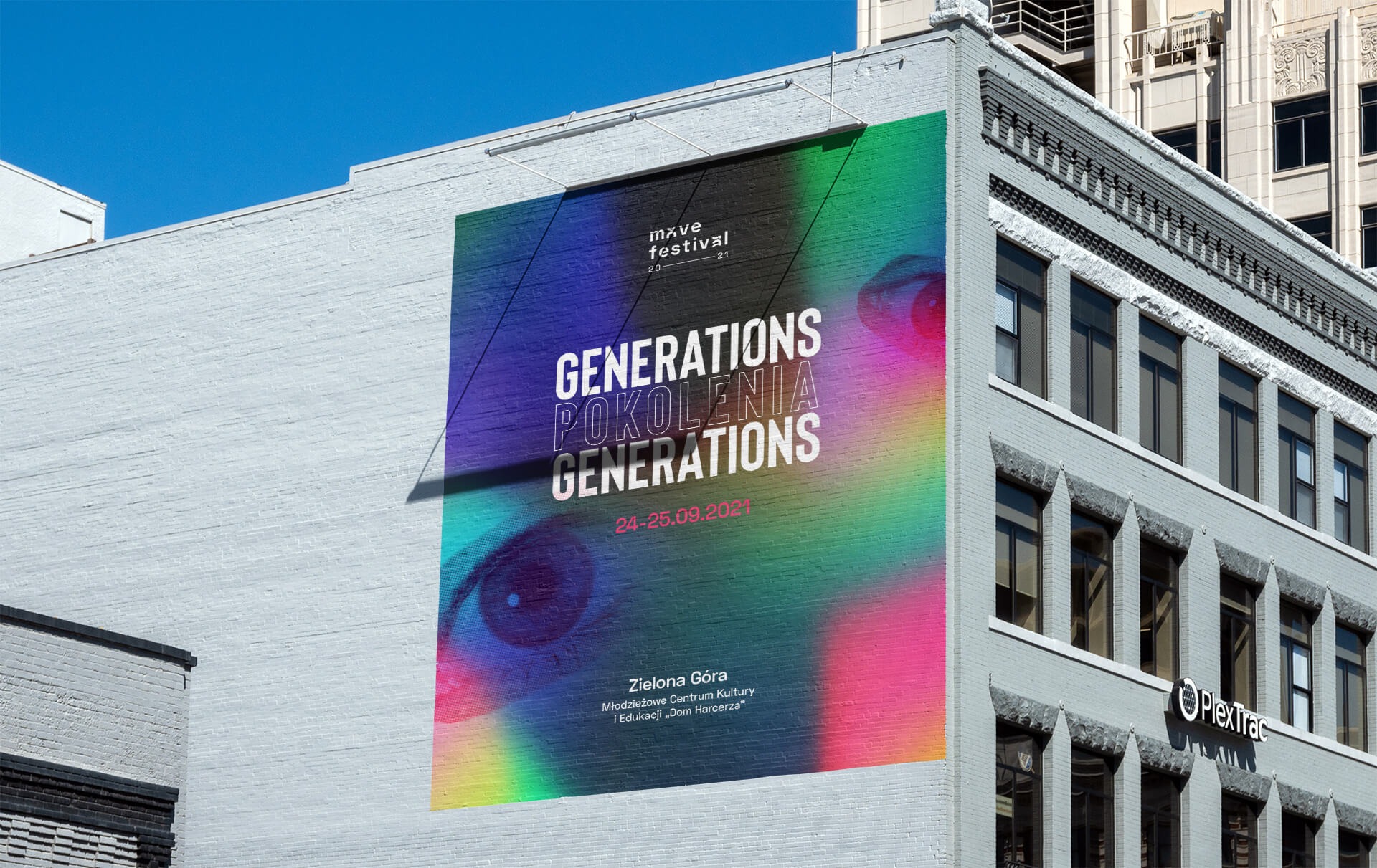 Wielkoformatowy plakat z tęczowym gradientem i motywem oka, promujący 'Move Festival Generations' w Zielonej Górze, umieszczony na ścianie budynku z cegły.