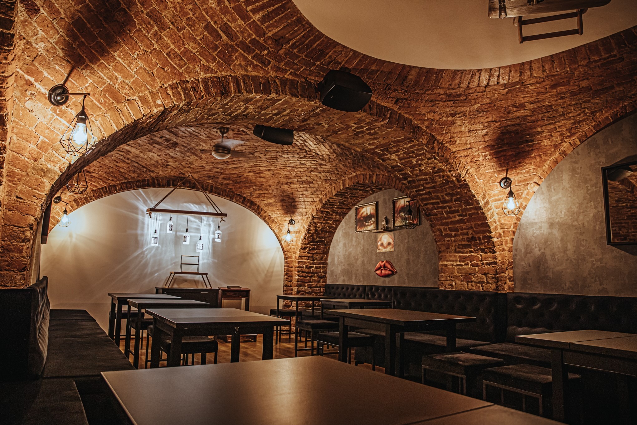 Klimatyczna sala VIP z ceglanym sklepieniem łukowym, oświetlona industrialnymi lampami. Ciemne meble i dekoracje ścienne tworzą unikalny nastrój.