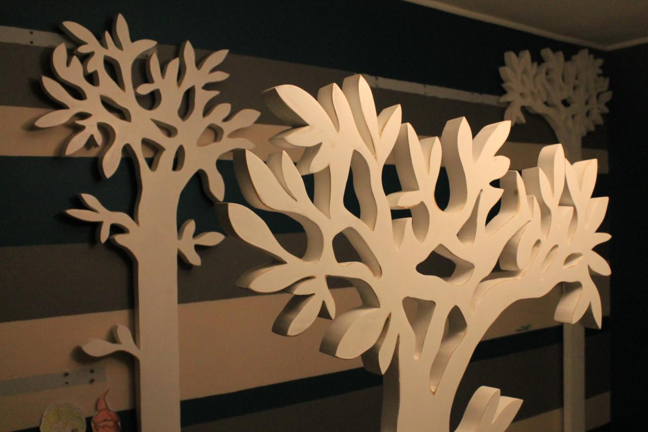 Dekoracyjne, przestrzenne drzewa z białego drewna na ścianie w poziome pasy, tworzące ozdobną kompozycję w pokoju dziecięcym.