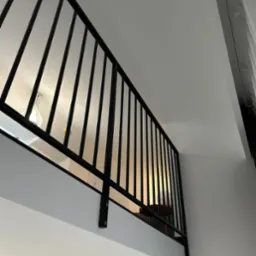 Nowoczesna czarna barierka na antresoli w jasnym wnętrzu, widok z dołu, z widoczną lampą i elementami wyposażenia kuchni w tle.