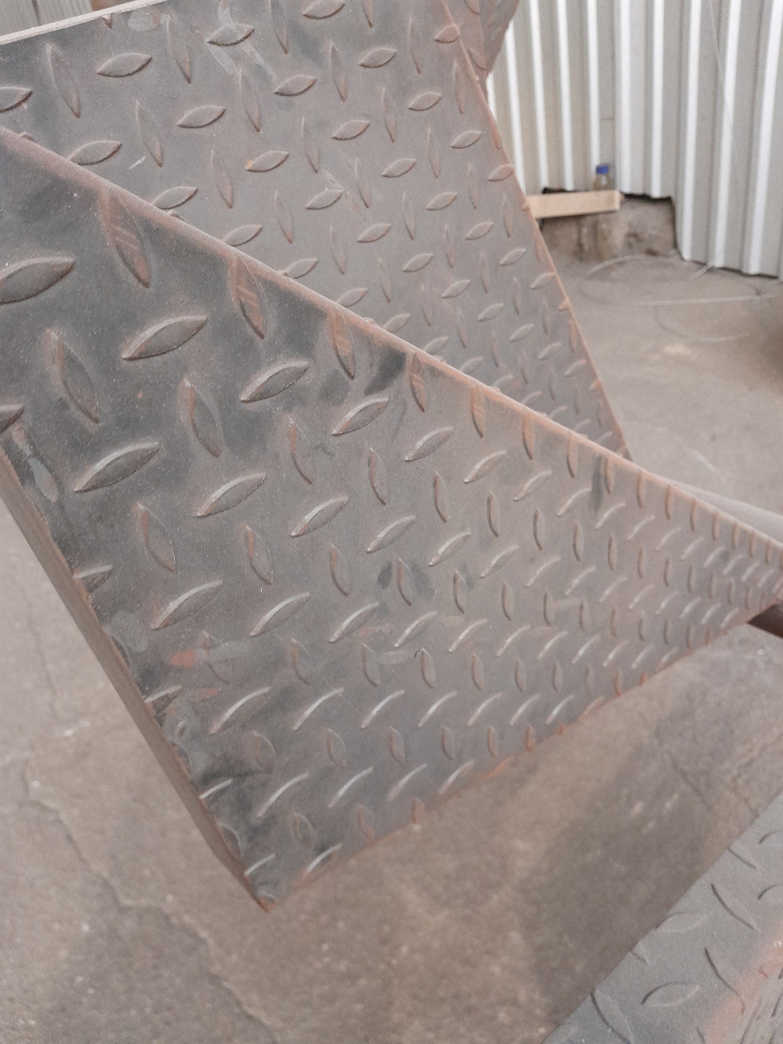 Fragment schodów metalowych z blachy ryflowanej, widoczne ślady korozji i spawania.