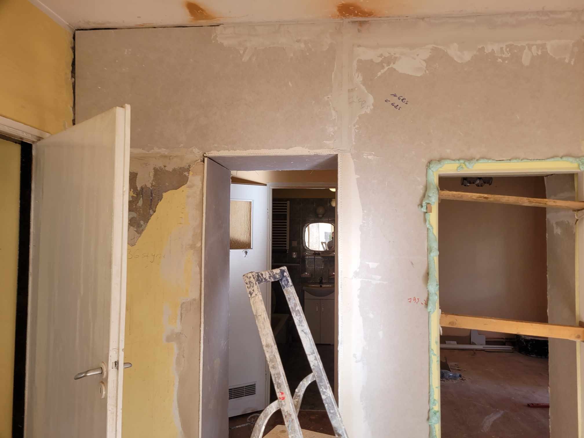 Wnętrze w trakcie remontu: widoczne fragmenty ścian z resztkami farby i gładzi, otwarte drzwi, drabina oparta o framugę oraz pianka montażowa uszczelniająca ościeżnicę.
