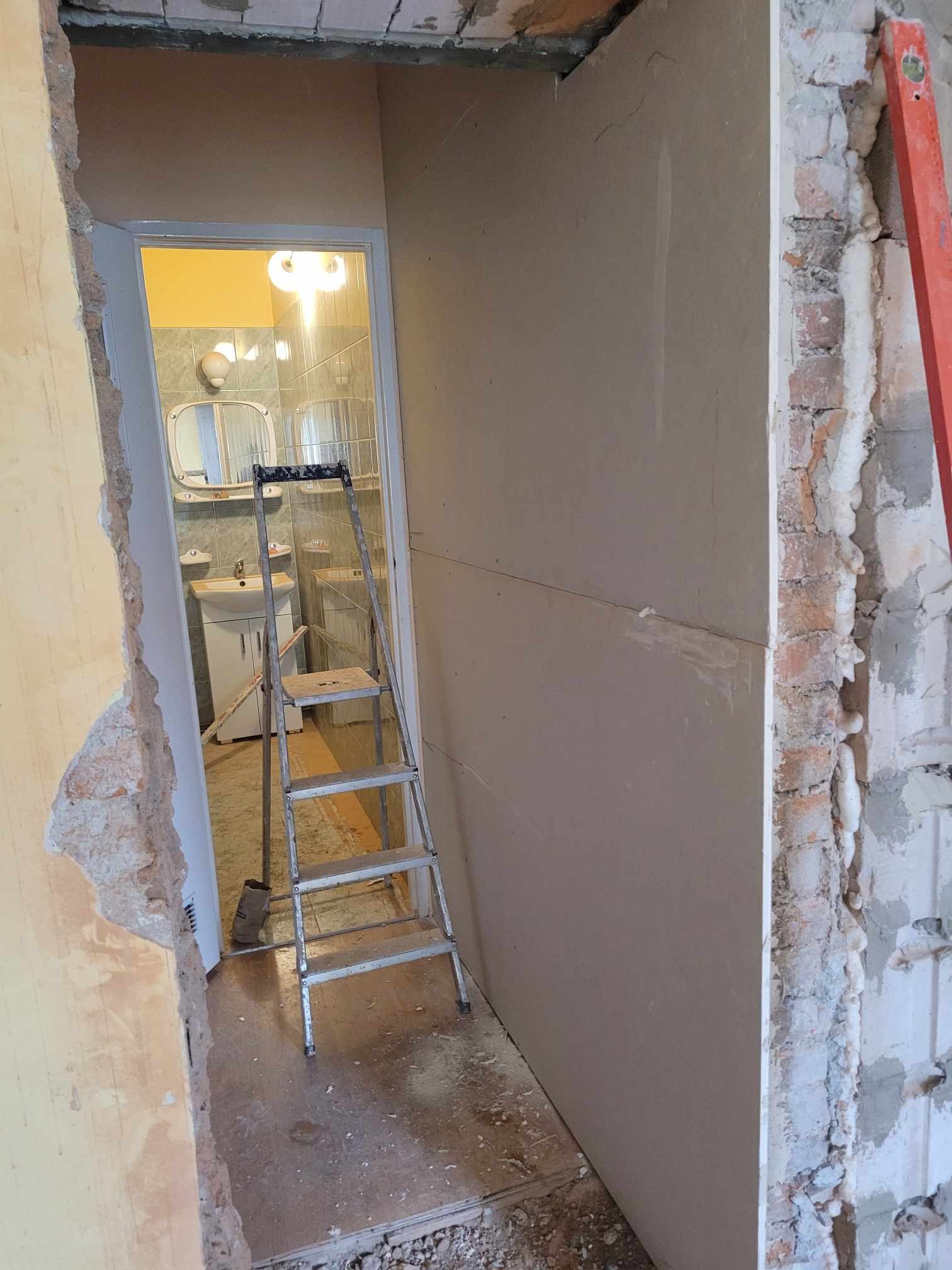 Remont łazienki w Kłodzku: widok przez otwór w ścianie na łazienkę w trakcie wykańczania, drabina oparta o ścianę, widoczne niedokończone ściany i instalacje.