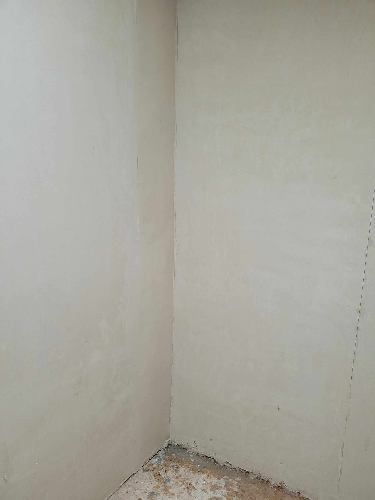Świeżo otynkowany narożnik pomieszczenia z widocznymi śladami po pracach wykończeniowych na podłodze.