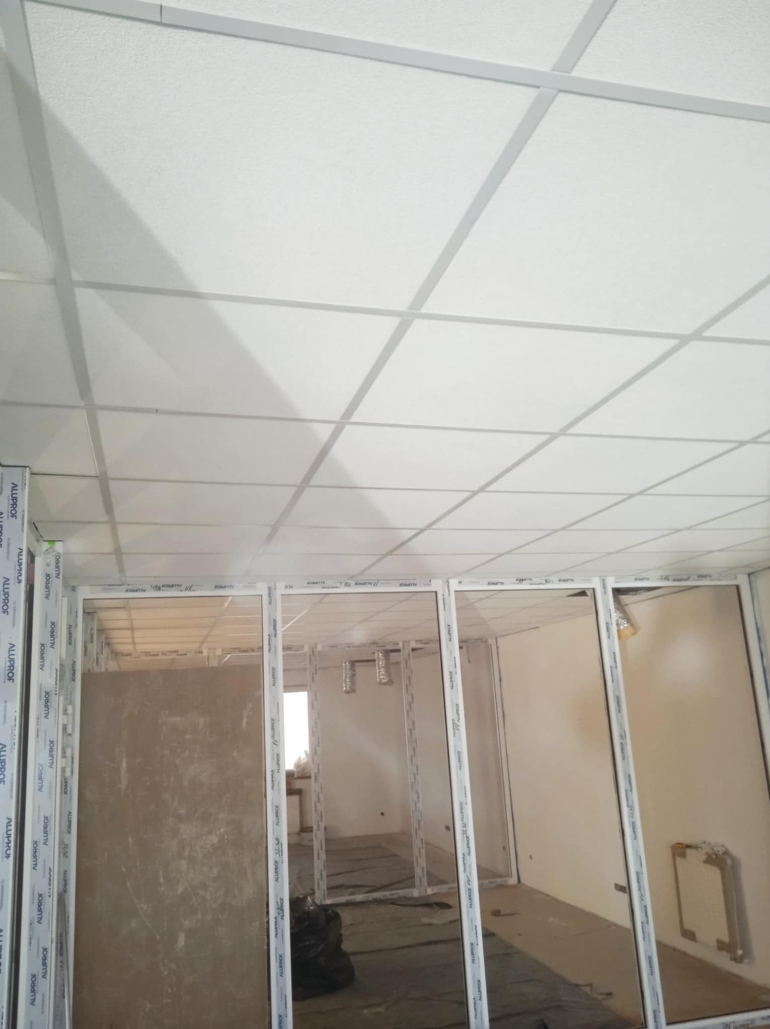 Montaż sufitu podwieszanego z widoczną konstrukcją i fragmentem ścian działowych w trakcie prac wykończeniowych. Widoczne profile aluminiowe.