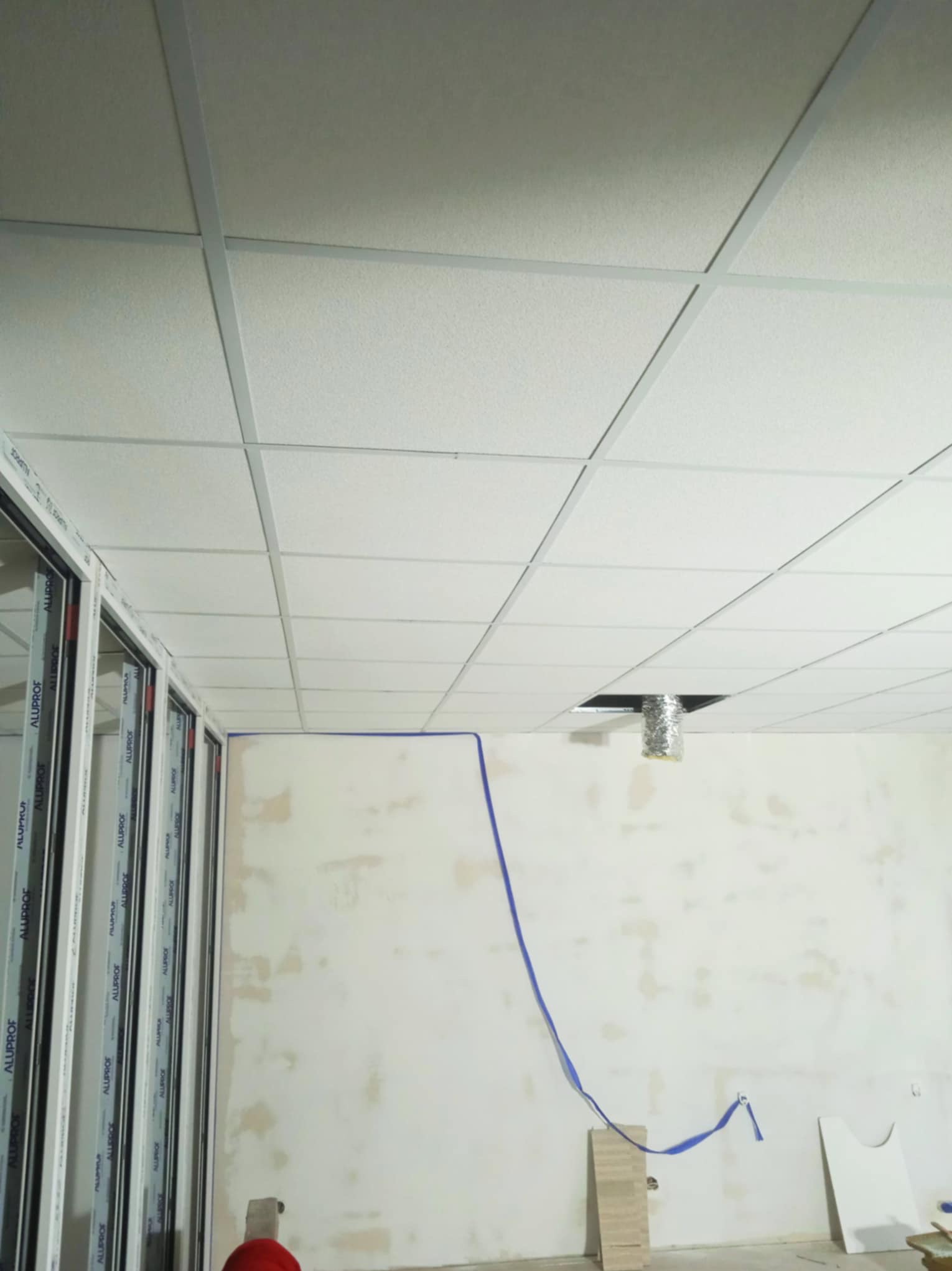 Montaż sufitu podwieszanego kasetonowego z widoczną instalacją wentylacyjną i przygotowaną ścianą do malowania. Widoczne profile okienne.