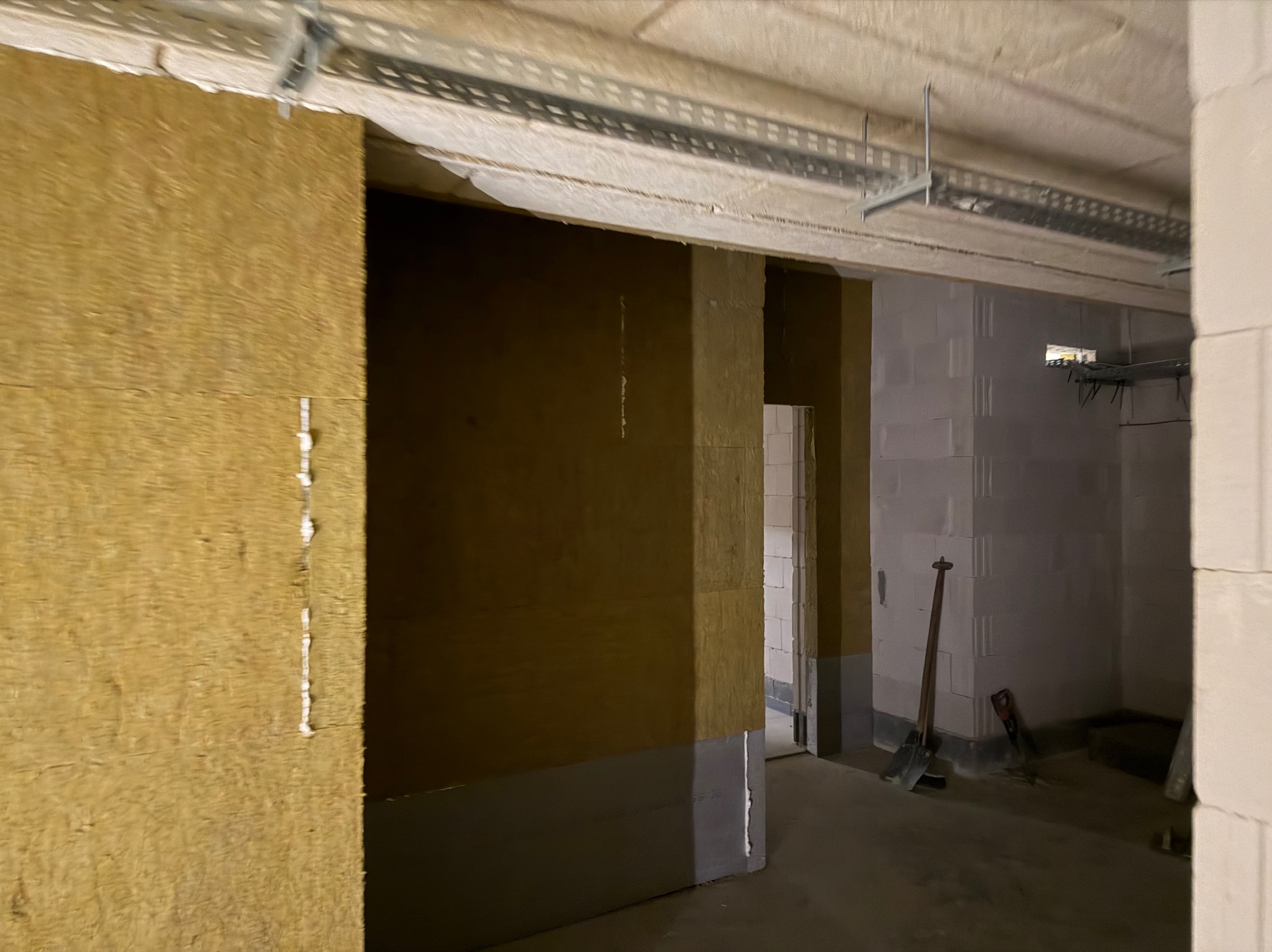 Wnętrze w trakcie prac wykończeniowych: ściany z izolacją z wełny mineralnej, widoczne profile pod sufitem i narzędzia budowlane. Surowy stan, przygotowanie do dalszych prac.