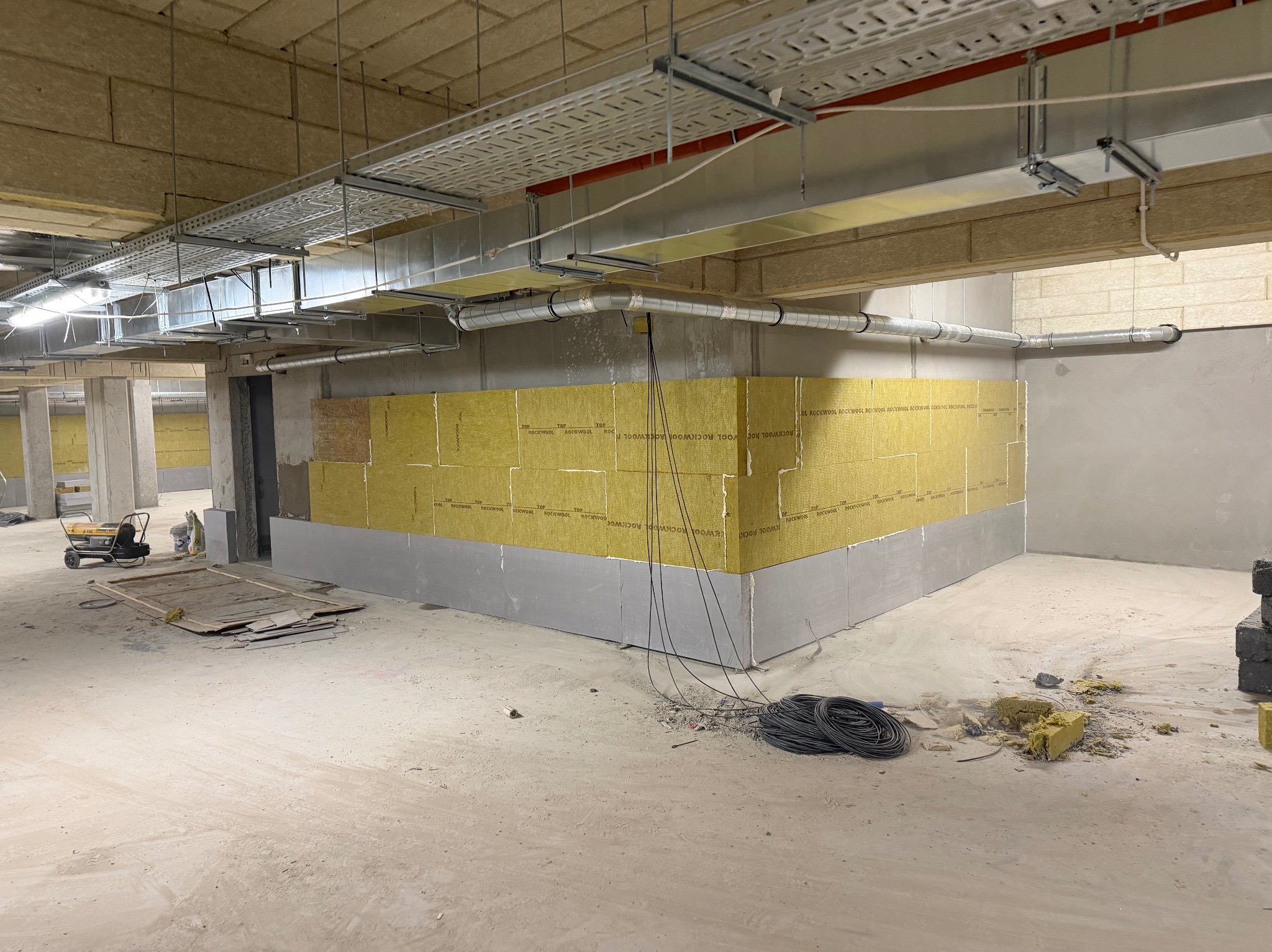 Ocieplenie ścian wełną mineralną w Mławie. Widoczne płyty izolacyjne Rockwool na ścianach, instalacje pod sufitem i narzędzia pracy. Etap prac wykończeniowych.