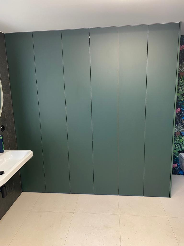 Zielona, matowa zabudowa wnękowa od podłogi do sufitu, widoczna umywalka i fragment tapety w kwiaty, realizacja w Szczytnie.