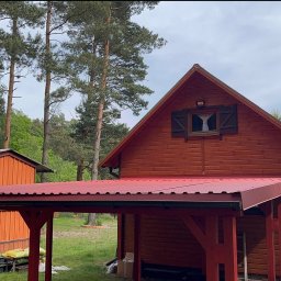 Łukasz Nowak - Czerwona drewniana altana przylegająca do domu z drewnianą elewacją. W tle widoczne drzewa i budynek gospodarczy w podobnej kolorystyce.