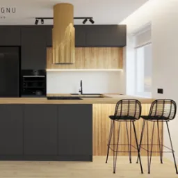 Nowoczesna kuchnia z czarnymi szafkami, drewnianym blatem i złotym okapem na tle ściany z obrazem twarzy