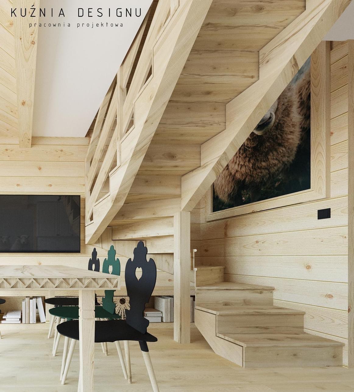 Drewniane schody w jasnym wnętrzu z boazerią, obraz z wizerunkiem żubra na ścianie, stół z krzesłami o dekoracyjnych oparciach, widoczny telewizor.