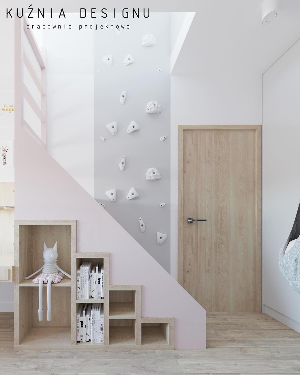 Pokój dziecięcy z elementami wspinaczki: białe chwyty na szarej ścianie, drewniane schody z półkami na książki i pluszową zabawką, jasna drewniana podłoga i drzwi.