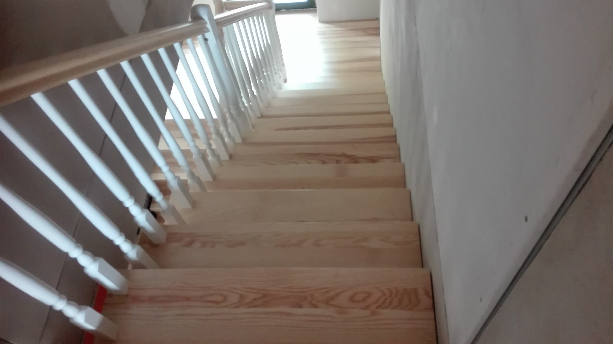 Jasne drewniane schody z białymi balustradami w surowym wnętrzu, widok z góry na stopnie.