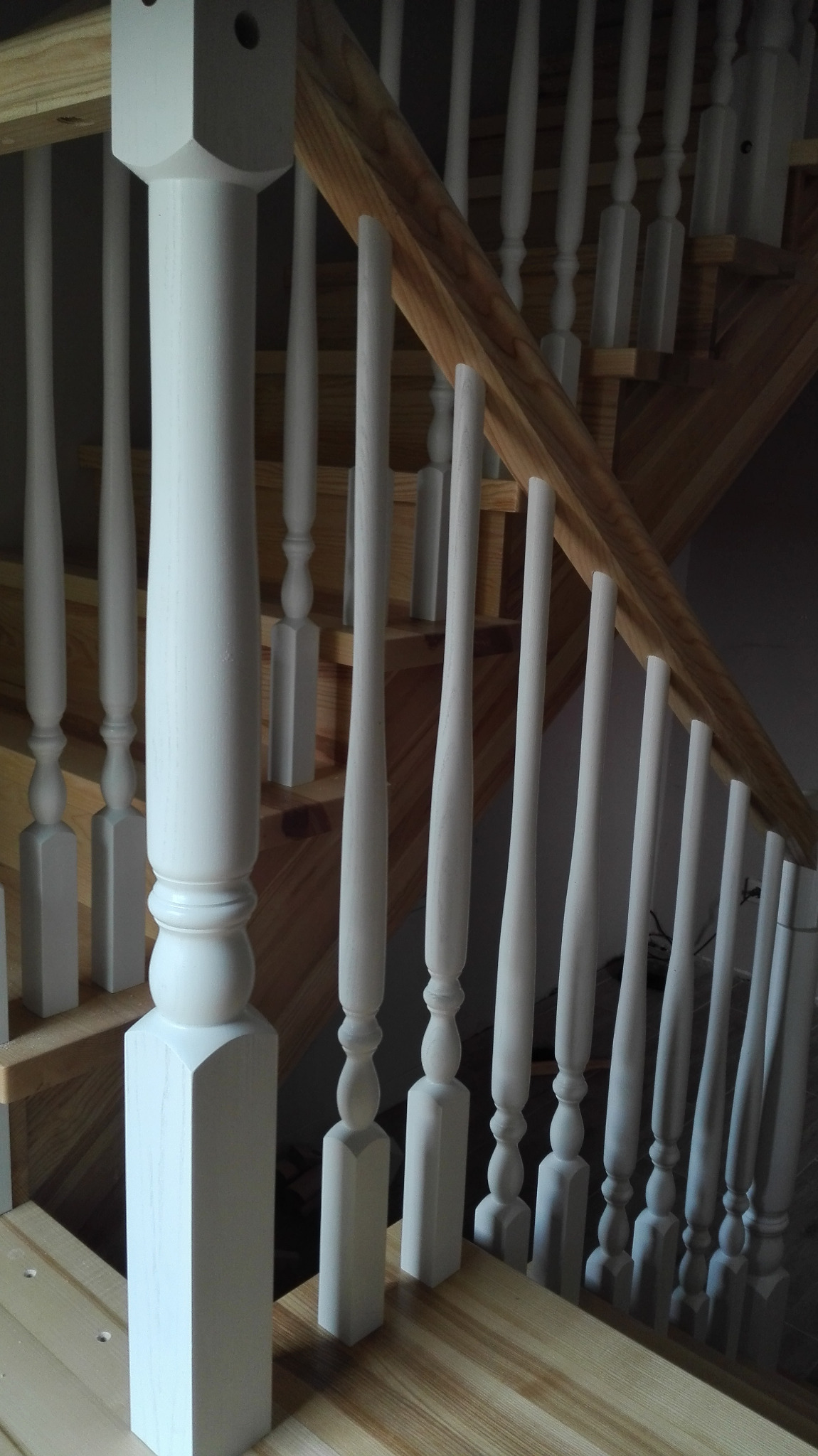 Fragment drewnianych schodów z białymi, toczonymi balustradami, widoczne z góry, z jasnymi drewnianymi stopniami i podstopnicami.