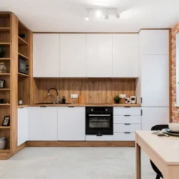 Jasna kuchnia z białymi frontami i drewnopodobnym wykończeniem, widok na ceglaną ścianę z oknem i stół z nakryciem.