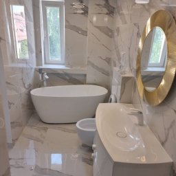 Maksbud Maksym Rosenko - Wykończona łazienka w marmurowej stylistyce z wolnostojącą wanną, bidetem, umywalką na szafce i okrągłym lustrem w złotej ramie, oświetlona nowoczesnymi lampami sufitowymi.