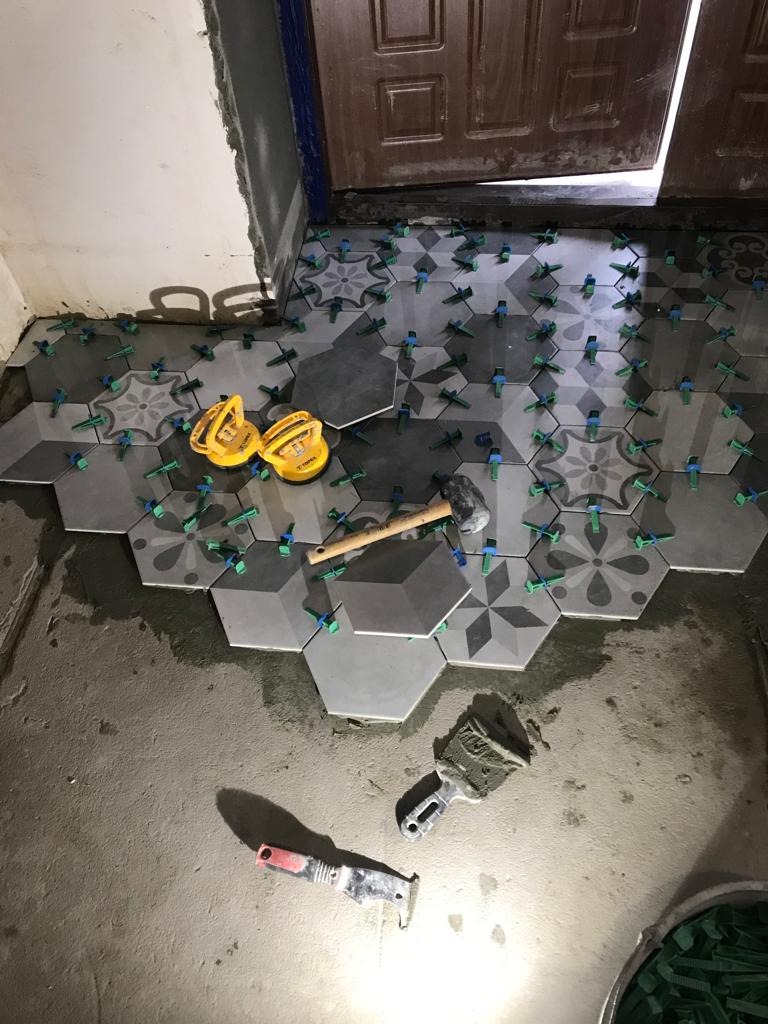 Układanie heksagonalnych płytek podłogowych z wzorami, używając przyssawek i klipsów poziomujących, w trakcie prac wykończeniowych w pomieszczeniu.