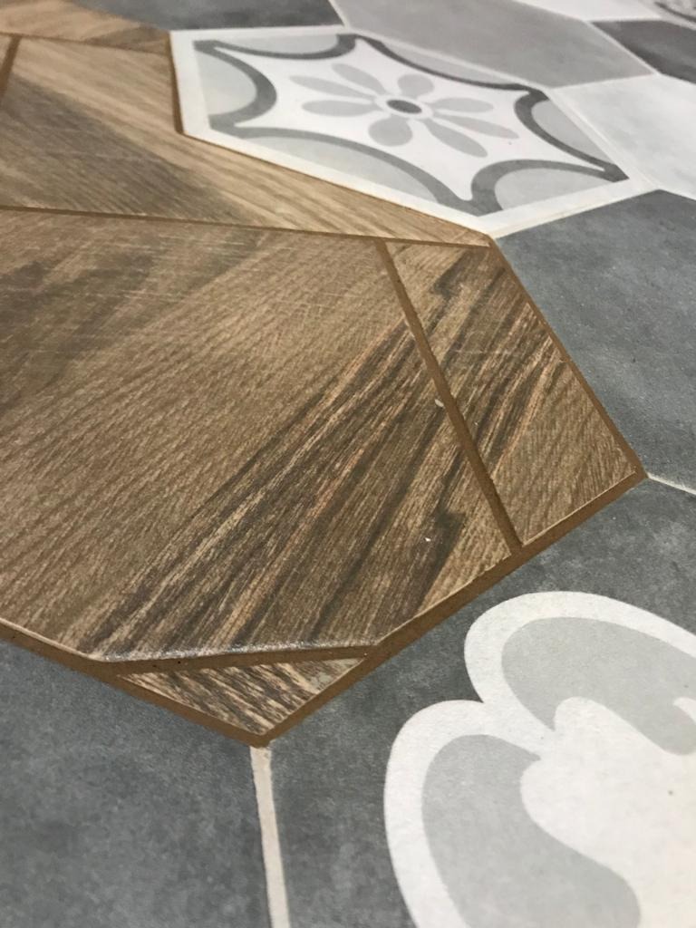 Wielobarwna podłoga z płytek o wzorze patchworkowym, łącząca imitację drewna i geometryczne motywy kwiatowe w odcieniach szarości i bieli, sfotografowana z bliska.