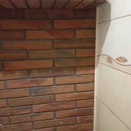 Fragment wykończonej łazienki z dekoracyjną ścianą z cegły klinkierowej i częściowo widoczną toaletą.