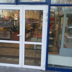 Białe, dwuskrzydłowe drzwi wejściowe do sklepu, widok z zewnątrz, z refleksami wnętrza sklepu i ulicy.