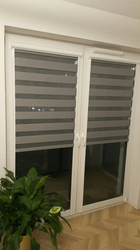 Zamontowane rolety dzień noc w oknie PCV we Wrocławiu, widok z wnętrza, z lewej strony doniczka z kwiatem.