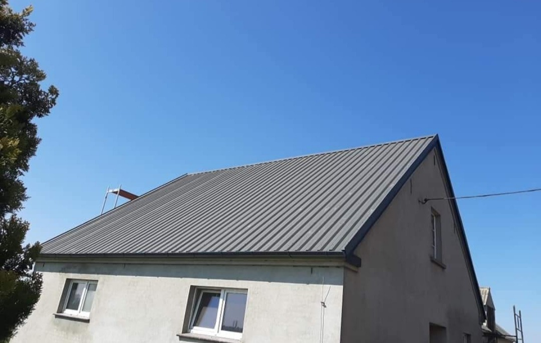 Dom jednorodzinny z nowym, szarym dachem z blachy trapezowej, widok z dołu na tle błękitnego nieba.