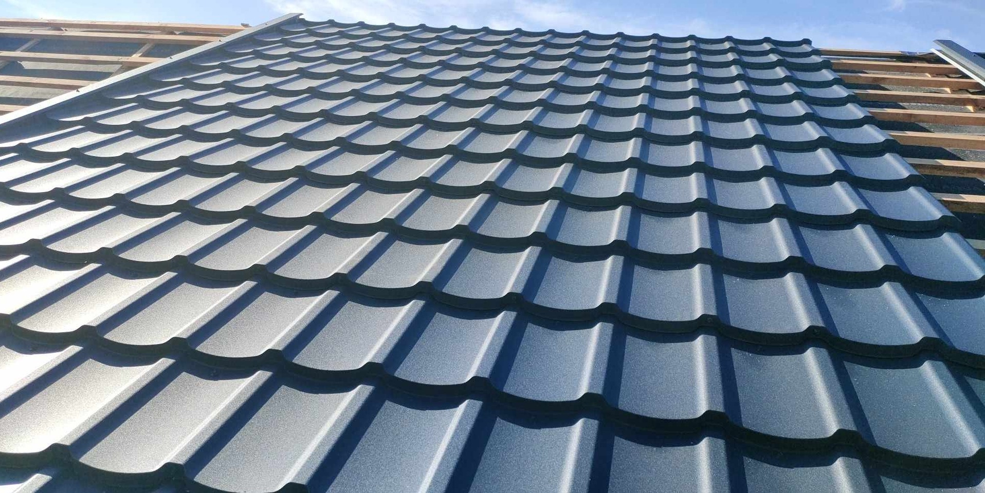 Nowe, szare blachodachówki ułożone na drewnianej konstrukcji dachu, widoczne niebo w tle.