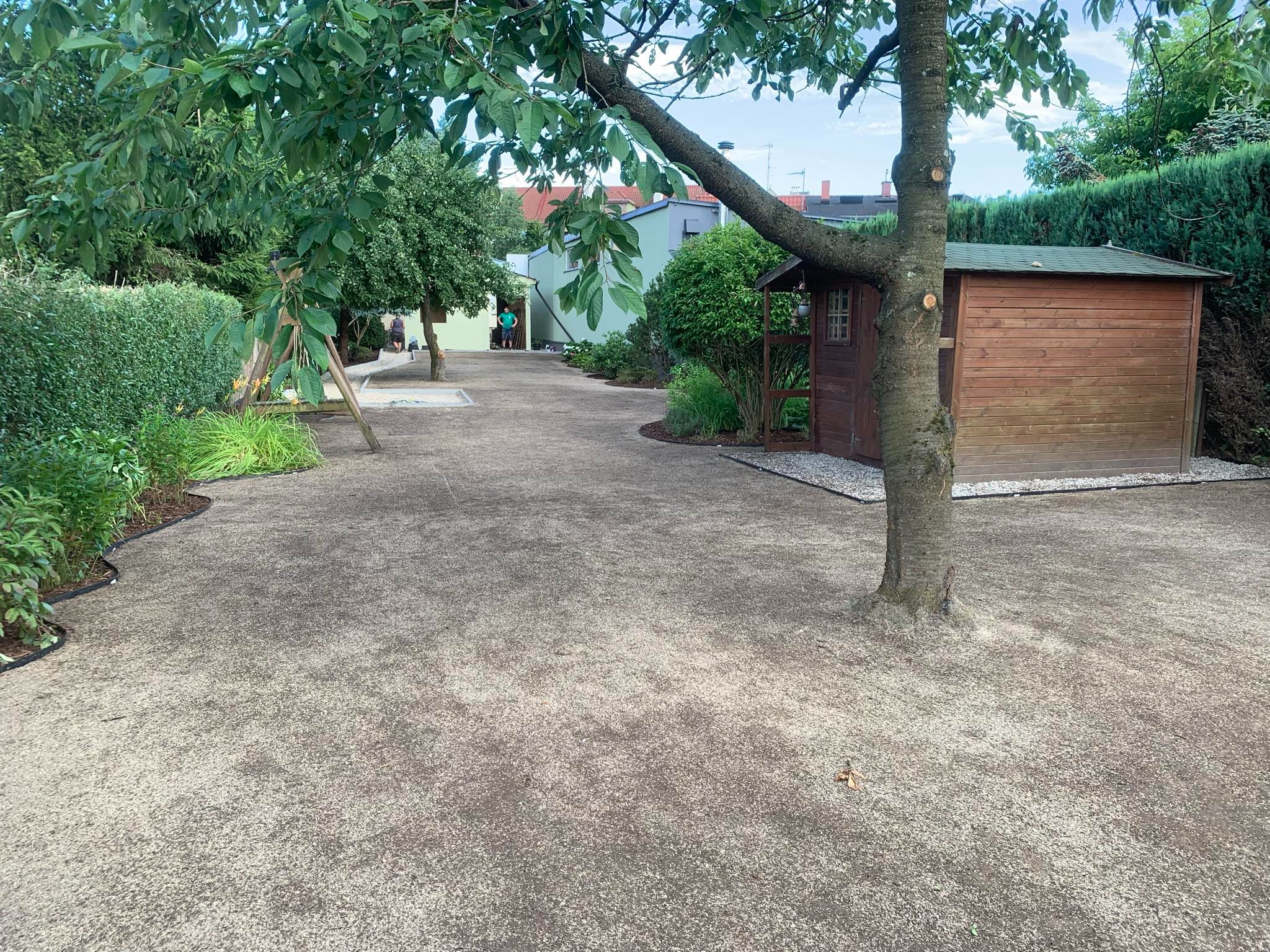 Przygotowany teren pod trawnik z rolki, widoczne obrzeża rabat, domek narzędziowy i drzewo na pierwszym planie.