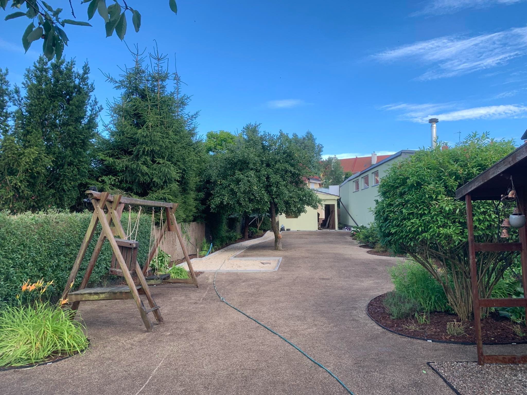 Przestronny ogród po wyrównaniu terenu, z przygotowanym podłożem pod trawnik, widoczne drzewa, krzewy, huśtawka i ścieżka z piasku.