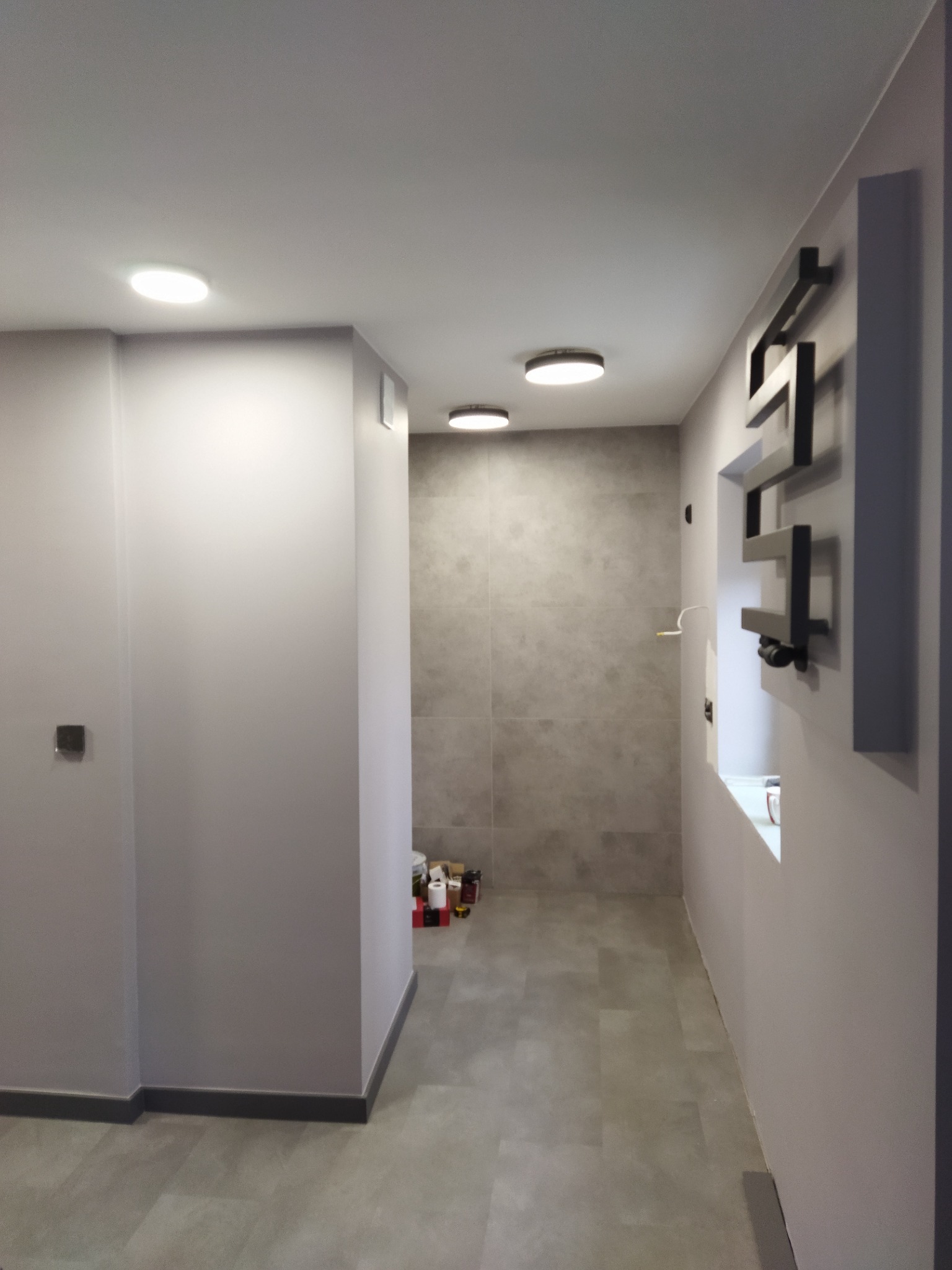 Nowoczesna łazienka po remoncie w Miedzianej Górze, z szarą glazurą, podwieszanymi lampami sufitowymi i dekoracyjnym grzejnikiem drabinkowym.