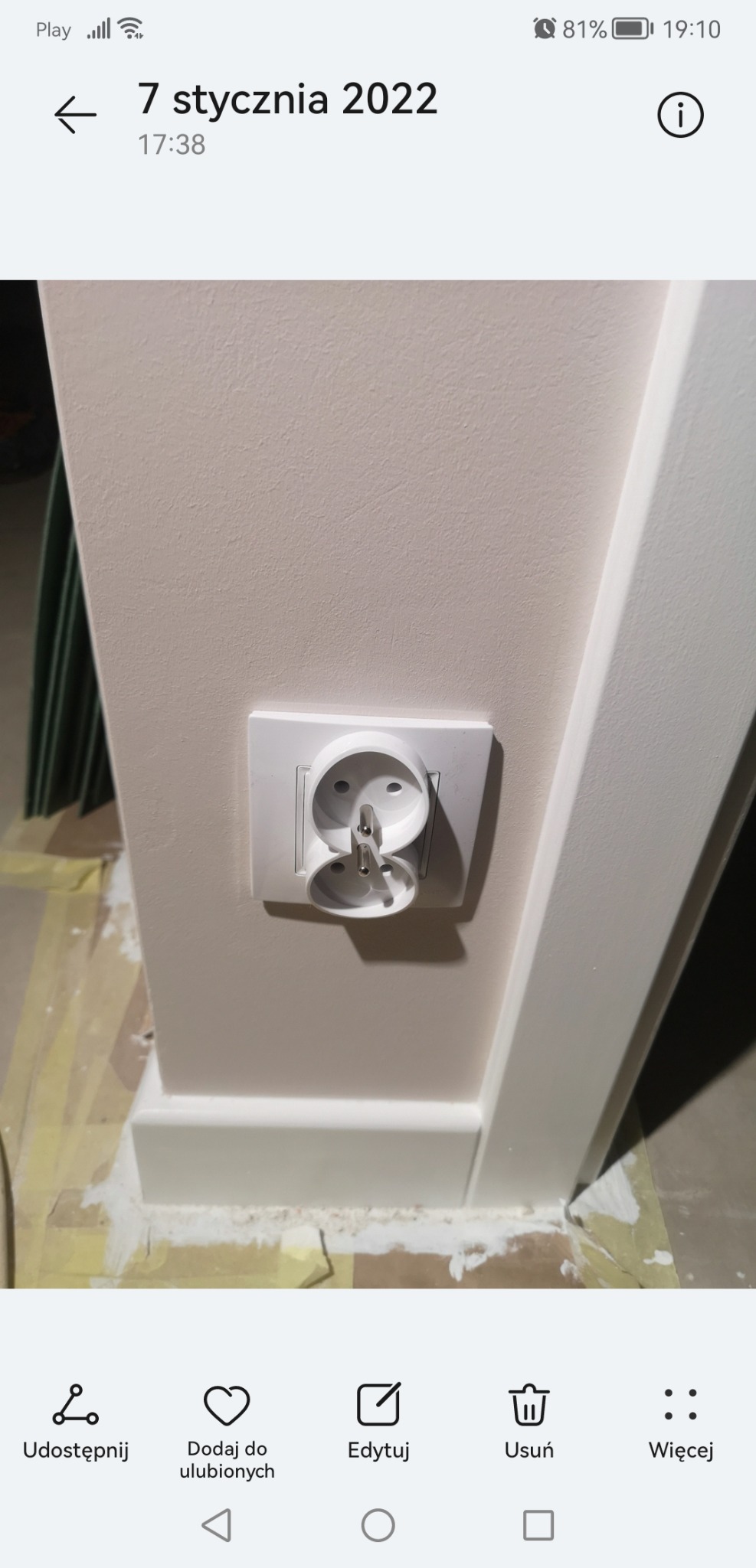 Podwójne gniazdko elektryczne zamontowane w ścianie pomalowanej na jasny kolor, widoczne ślady uszczelniania wokół listwy przypodłogowej, co sugeruje prace wykończeniowe w trakcie.