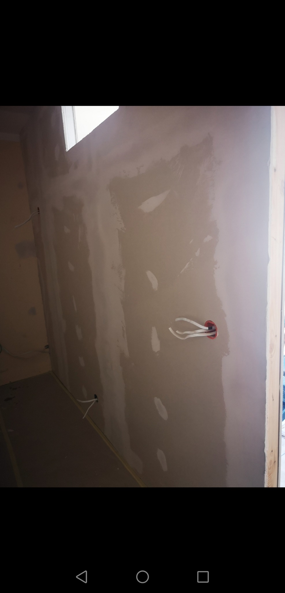 Ściana po wstępnym szpachlowaniu z widocznymi przewodami elektrycznymi wystającymi z puszki, przygotowana do dalszych prac wykończeniowych.