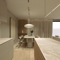 Marta Fibich - Beżowa kuchnia z wyspą i stołem jadalnym w tle, oświetlona nowoczesnymi lampami. Minimalistyczny design z drewnianą podłogą i dekoracjami.