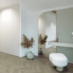 Nowoczesna łazienka z toaletką, okrągłym lustrem, puszystym stołkiem, parkietem ułożonym w jodełkę i dekoracyjnymi trawami w wazonie.