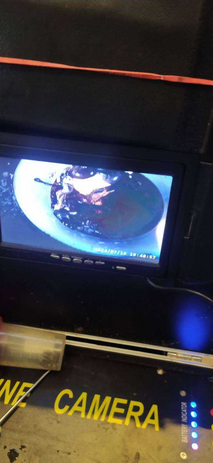 Ekran kamery inspekcyjnej z widokiem wnętrza rury kanalizacyjnej podczas badania, w tle widoczny napis 'LINE CAMERA' i diody wskazujące stan baterii.