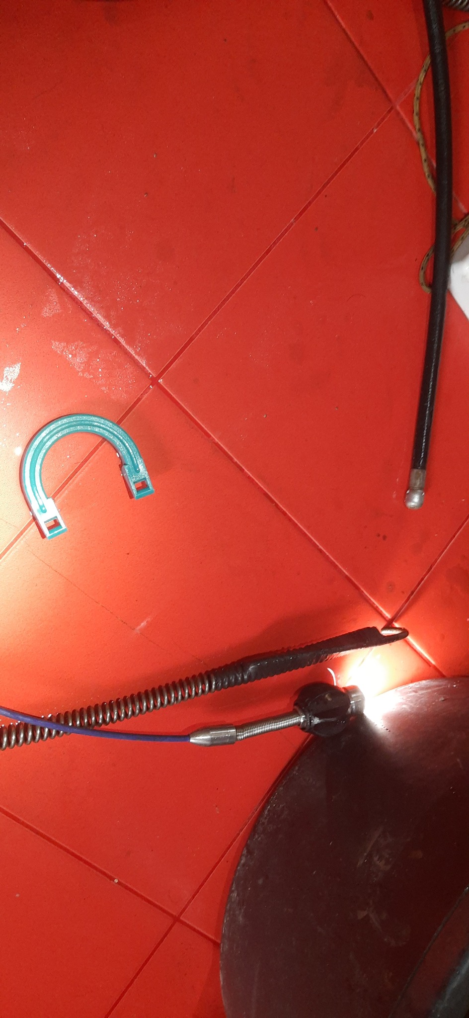 Sprężyna kanalizacyjna z niebieskim rdzeniem, uchwyt i końcówka do udrażniania na czerwonej, kafelkowanej powierzchni podłogi.