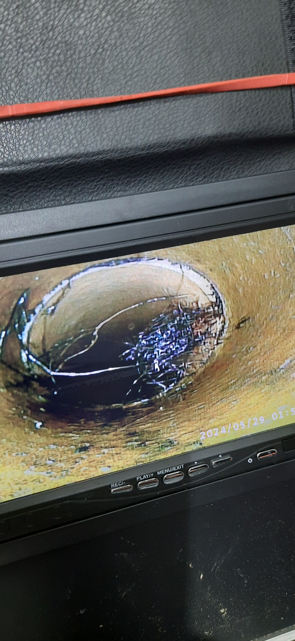 Widok z kamery inspekcyjnej wewnątrz rury kanalizacyjnej, widoczne zanieczyszczenia i osady, data i godzina na ekranie monitora kamery.