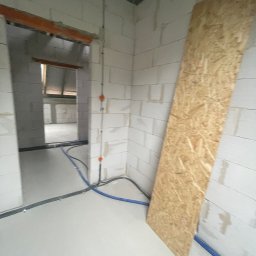 RM Technology - Surowy stan wnętrza z widocznymi przewodami elektrycznymi w peszlach na ścianach z betonu komórkowego. Na podłodze leży płyta OSB.