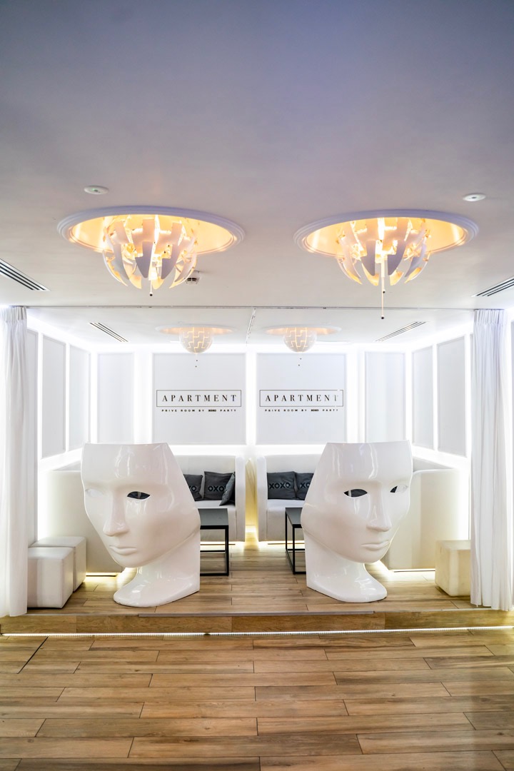 Białe, teatralne maski-krzesła w przestrzeni eventowej z drewnianą podłogą i designerskimi lampami sufitowymi.